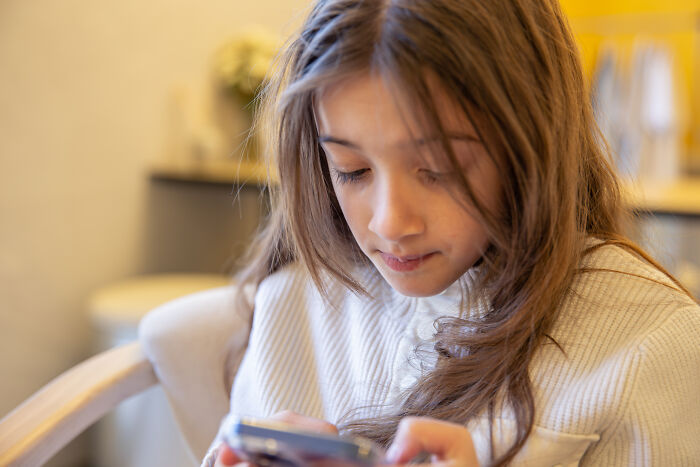 Young girl looking upset while reading messages on her phone, illustrating daughter found dad cheating texts concept. - 1