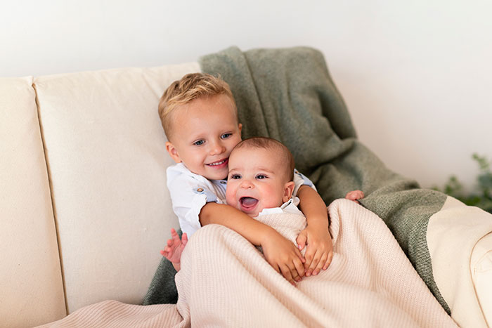 Two young siblings sitting on a couch wrapped in blankets, showing a caring babysitting moment.