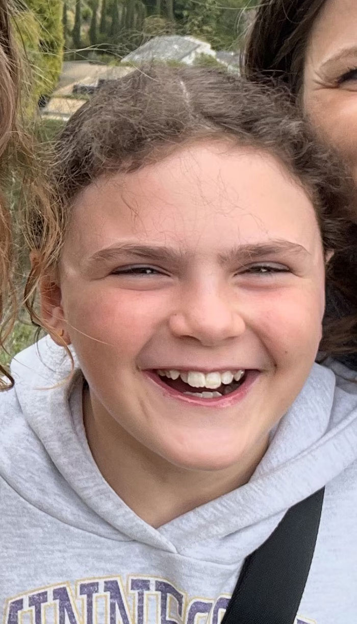 Smiling young girl wearing a gray hoodie outdoors, related to Minneapolis school attacker mother not cooperating with cops debate.