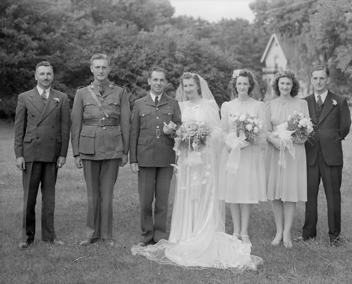 1940s wedding party posing outdoors with bride, groom, bridesmaids, and military servicemen in a moving wedding photo.