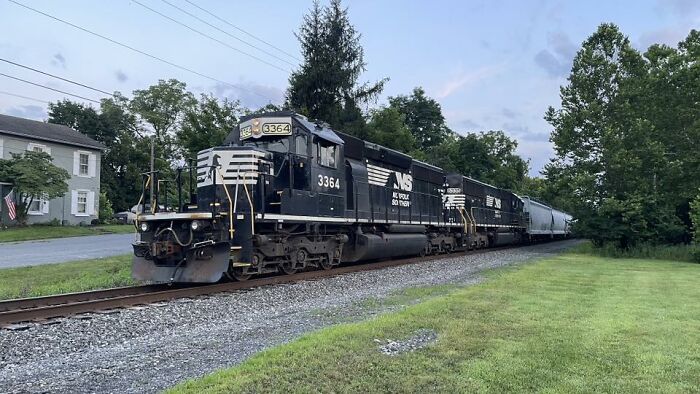 Black Norfolk Southern freight train with multiple engines traveling on tracks through a green rural area, appealing to any man.