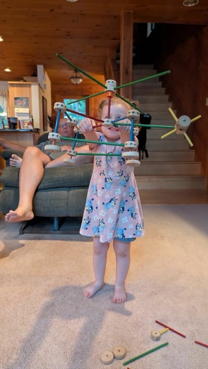 Young child excitedly holding a colorful wooden toy structure indoors, capturing a moment for any man to enjoy.