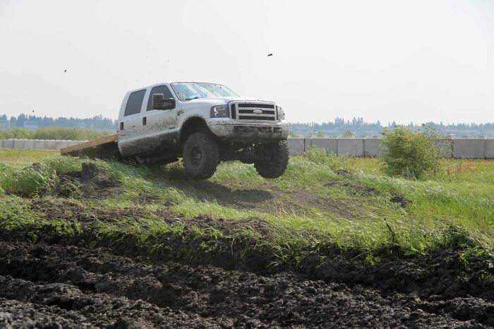 White off-road truck catching air over muddy terrain, showcasing thrilling moments any man would be excited to see.