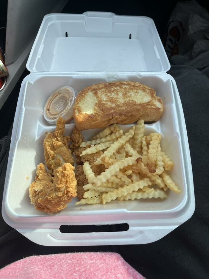 Takeout meal with fried chicken tenders, crinkle-cut fries, toasted bread, and dipping sauce in a container any man would be excited to see.
