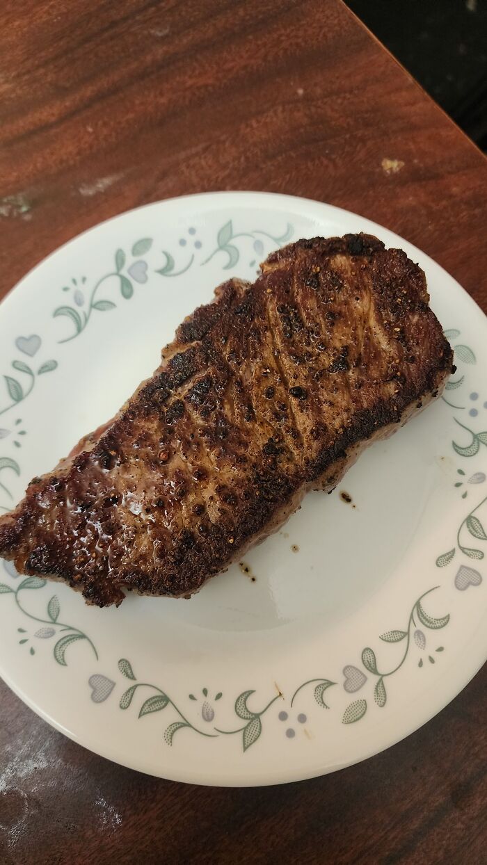 Grilled steak on a white plate with floral pattern, showcasing a juicy and well-seasoned piece of meat any man would be excited to see.