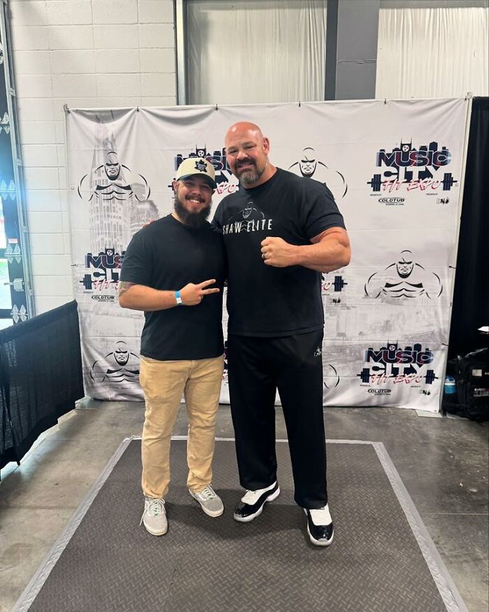 Two men smiling and posing together at a fitness event, showcasing strength and camaraderie for any man excited to see these pics.