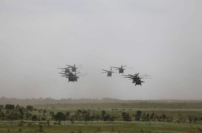 Military helicopters flying low over a green field during an overcast day, a scene any man would be excited to see.