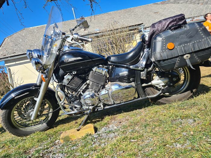 Black cruiser motorcycle parked on grass near a house, showcasing a classic design any man would be excited to see.