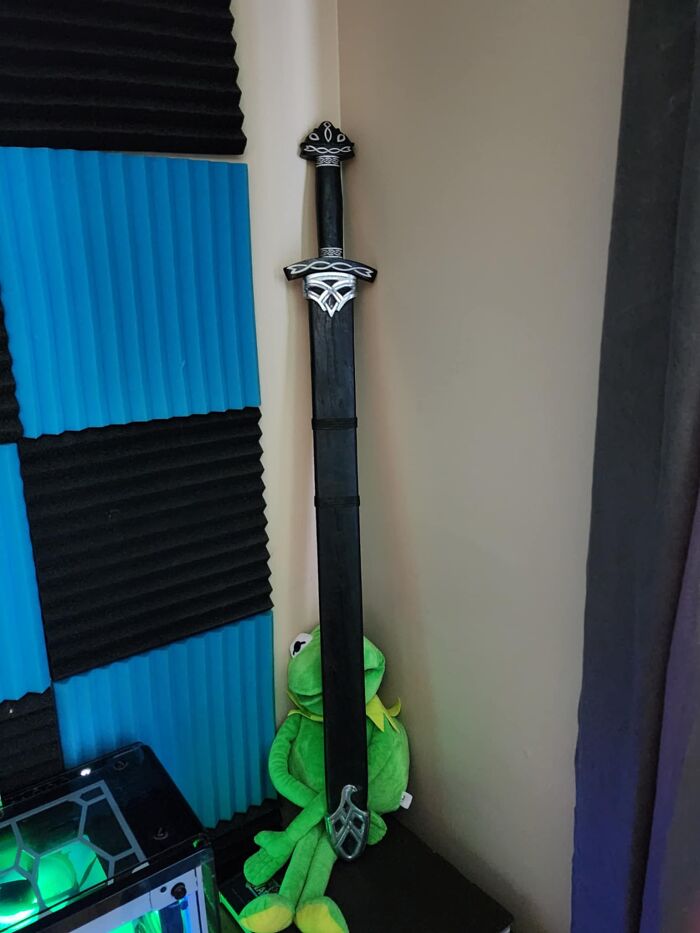 Black decorative sword leaning in a corner with blue and black foam panels and a green plush toy nearby, appealing to men.