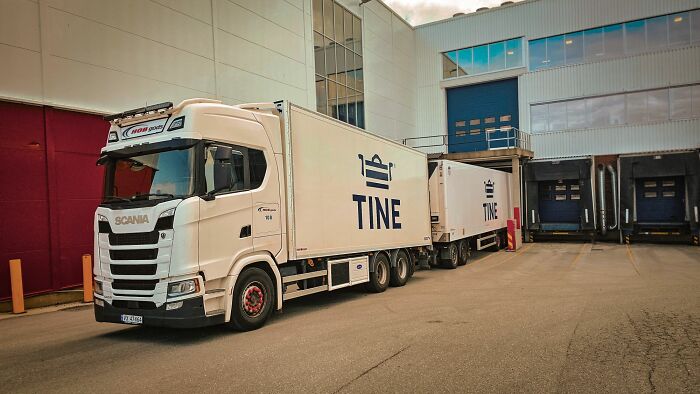 White Scania truck with TINE trailers parked outside a warehouse, showcasing any man would be excited transport scene.