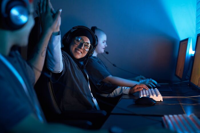 Teen gamers smiling and high-fiving while playing on computers, representing the smartest kids in their class.