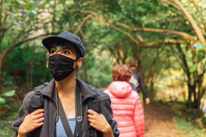 Person wearing a black mask and cap hiking in the woods with others, capturing the feeling of sleepless nights after woods experience - 12