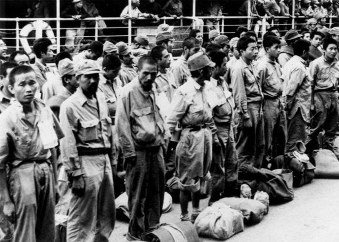 Black and white photo of prisoners standing in a line with bags, depicting a historical event of people who actually survived.