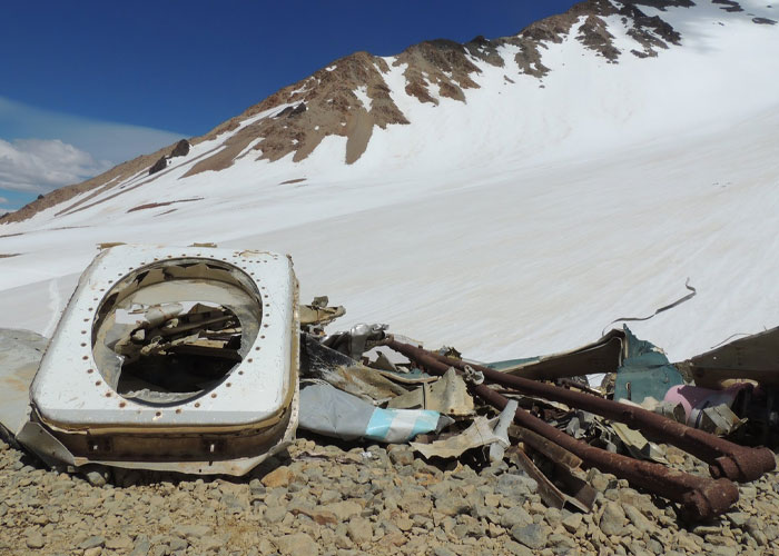 Wreckage of a historical plane crash on rocky terrain with snow-covered mountains in the background, survival evidence.