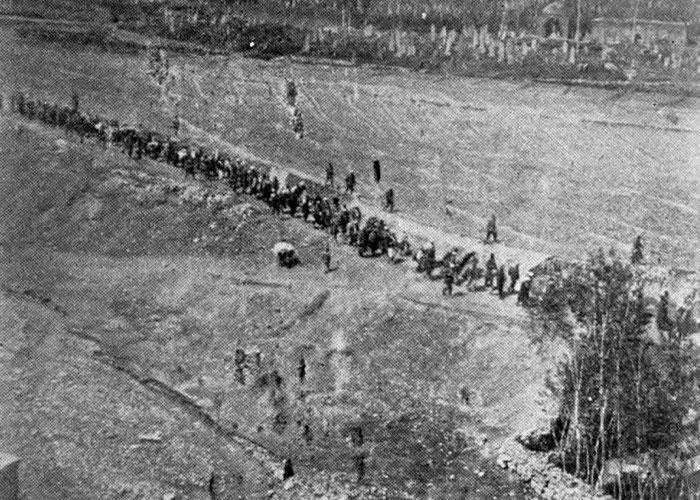 Black and white aerial view of people walking in a long line near barren land, representing historical survival events.