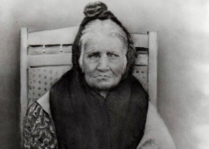 Elderly woman sitting in a wooden chair, representing survivors of unbelievable historical events from the past.