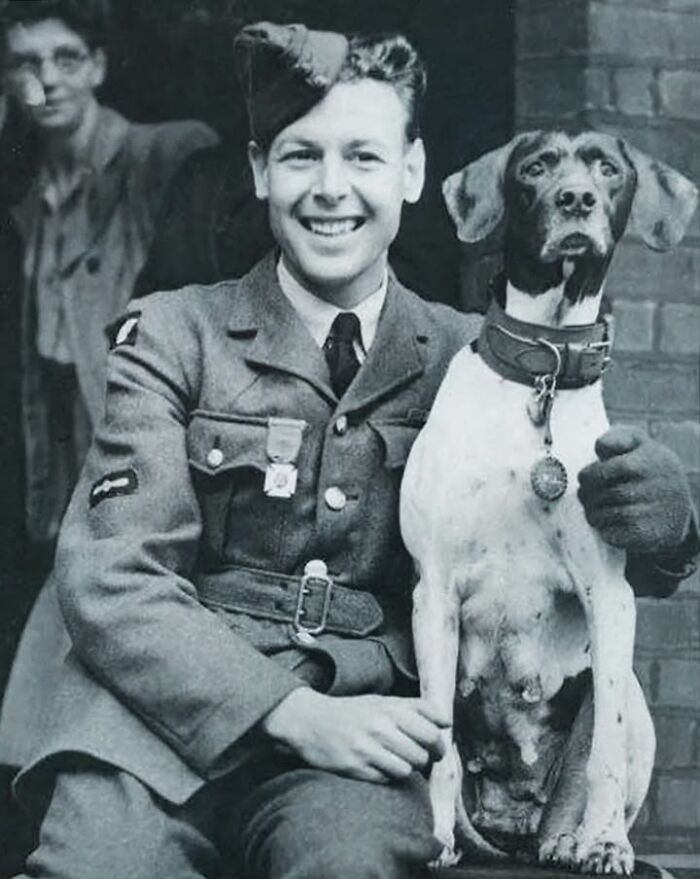 Smiling soldier posing with his pet dog wearing a collar and medal in a fascinating historical photo of pets.