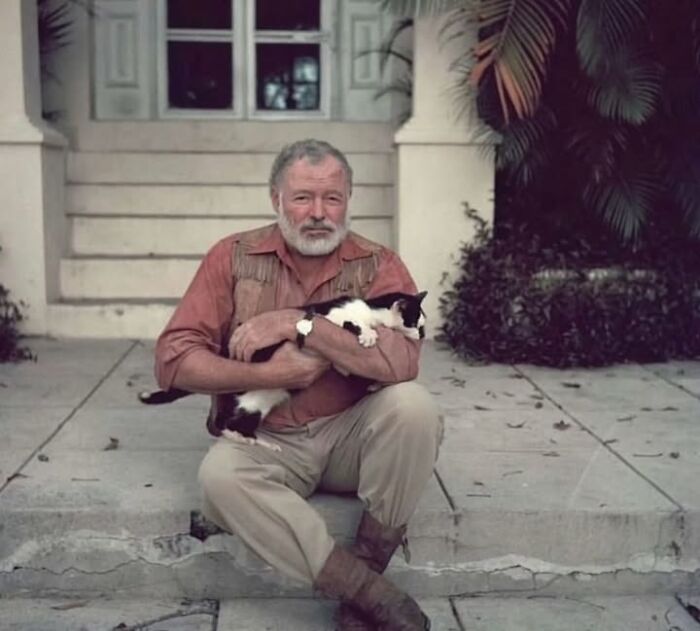 Man sitting on steps holding a black and white cat in a vintage setting, showcasing historical photos of pets.