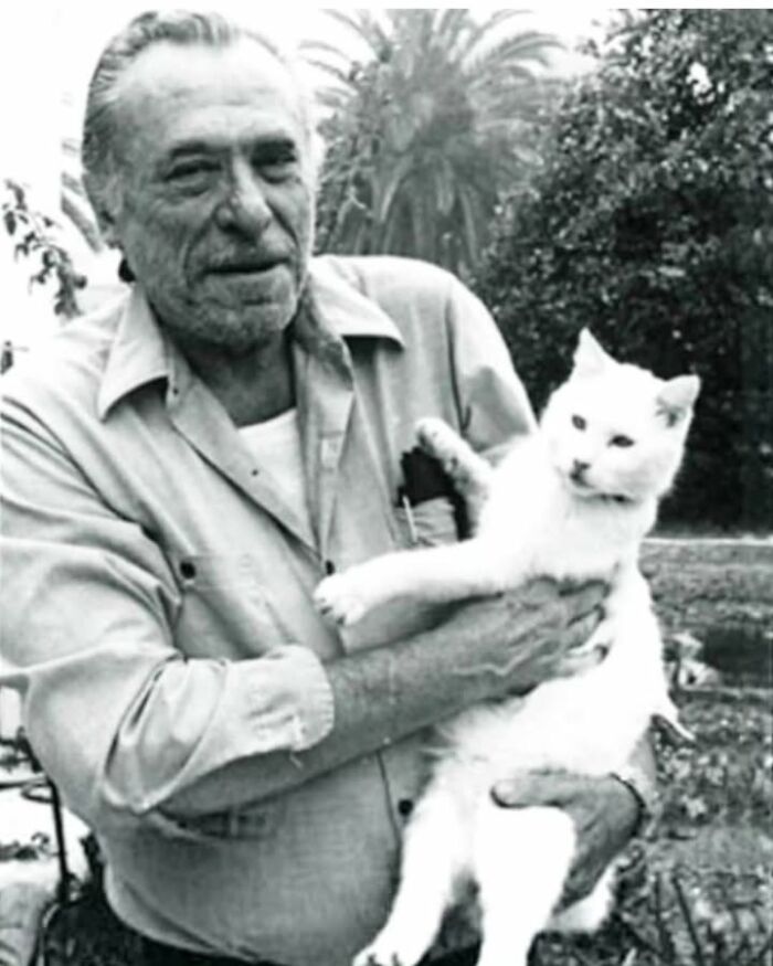 Black and white historical photo of a man holding a white cat outdoors, highlighting pets in history.