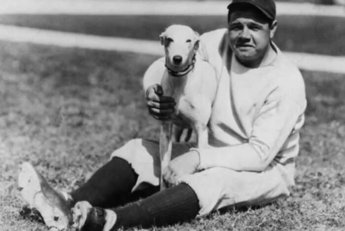 Black and white photo of a man sitting on grass holding a dog, showcasing historical photos of pets and their bond.