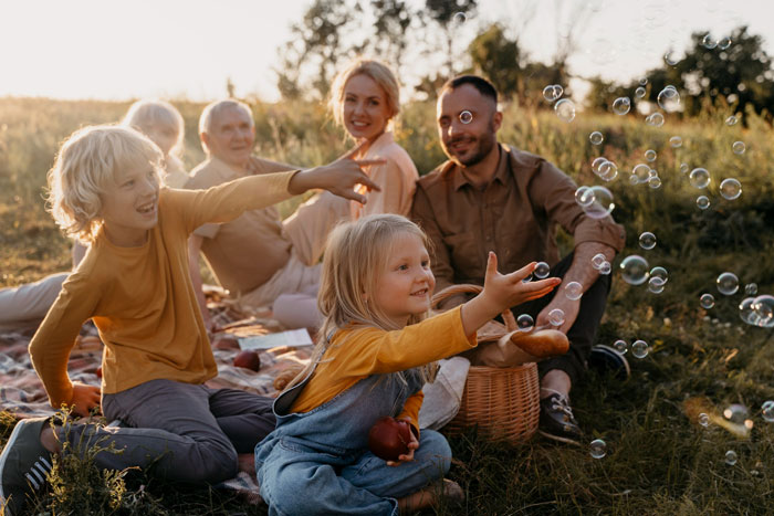 Childfree woman enjoying peaceful outdoor picnic while relatives and children play nearby during vacation getaway.
