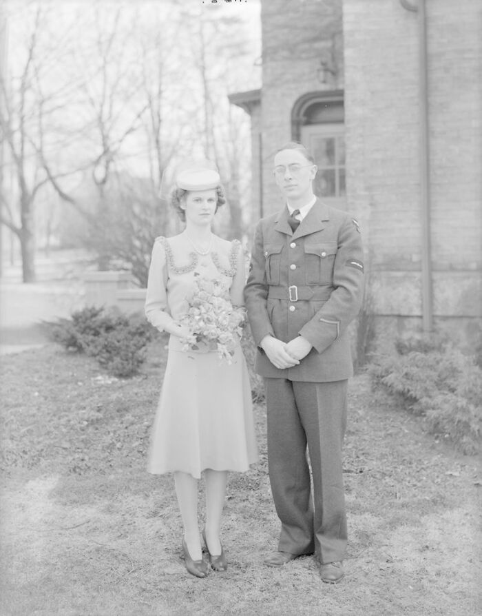 Bride in 1940s dress holding bouquet standing beside groom in military uniform in moving wedding photo from war era.