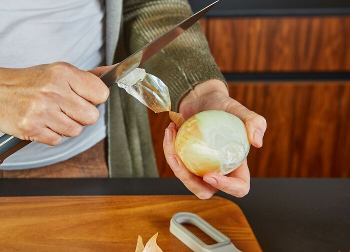 Person peeling onion with a knife in kitchen, illustrating restaurant workers needing a bonus for tough orders.