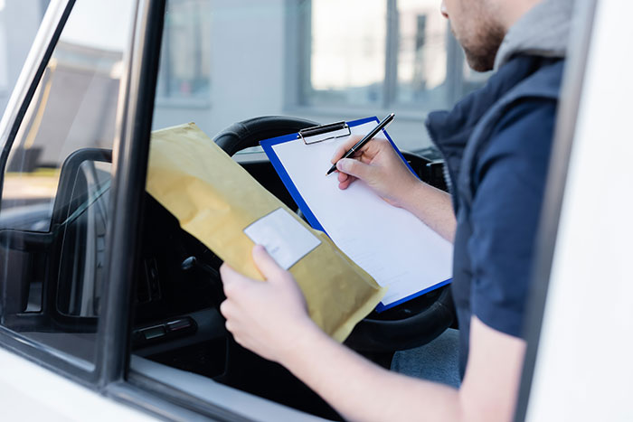 Man holding envelope and writing on clipboard inside vehicle, illustrating 23 more follow ups for dealing with petty HOA disputes.