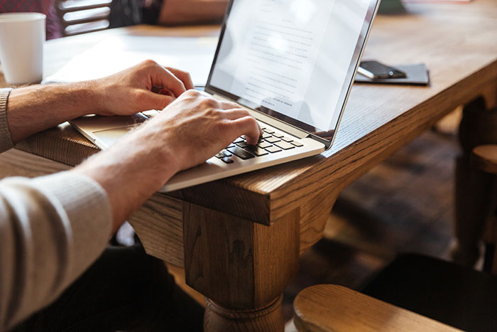 Man typing on laptop at wooden table focused on follow ups dealing with petty HOA disputes and fire with fire approach
