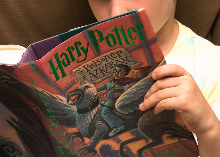 Child holding Harry Potter book, reading Harry Potter and the Prisoner of Azkaban in a cozy setting.