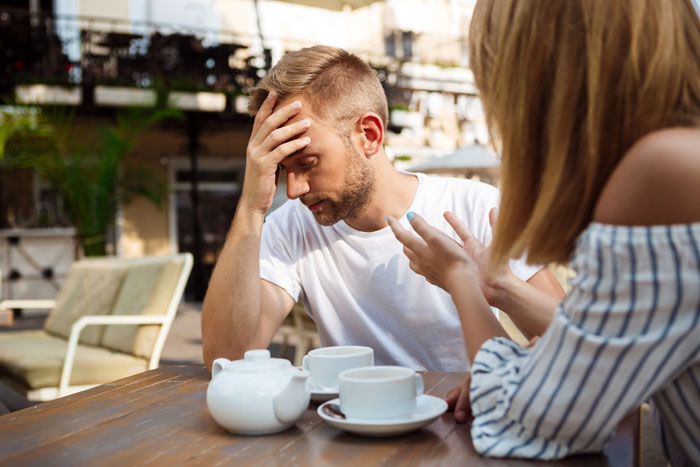 Man looking stressed while woman talks to him at an outdoor cafe, relating to wife surprise visitor and pregnancy claims. - 14