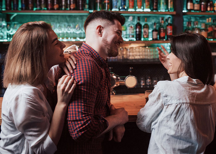Woman and two friends at bar, man smiling and engaged in conversation, illustrating changes in husband since wedding.
