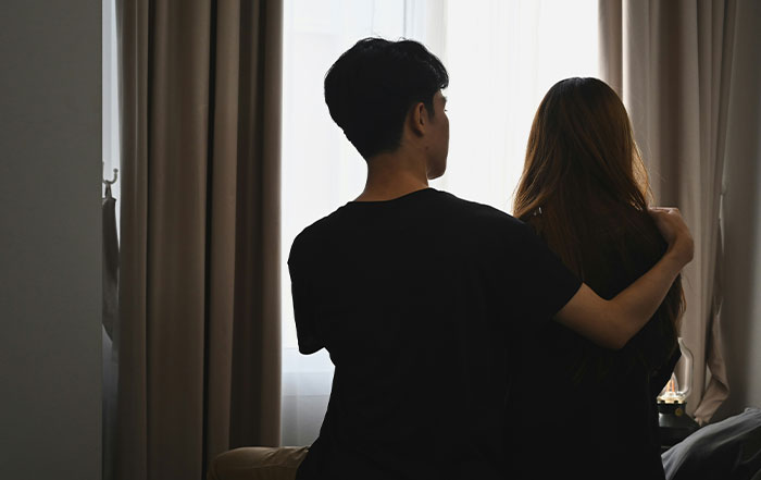 Man and woman sitting together near window, man comforting wife, reflecting tension in marriage and divorce demands. Man and woman sitting together near window, man comforting wife, reflecting tension in marriage and divorce demands.