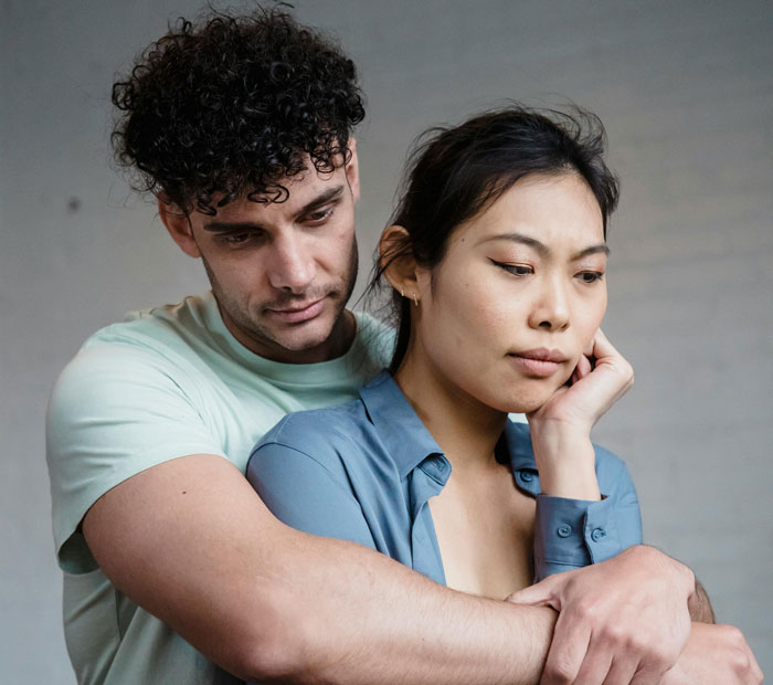 Husband and wife in a tense embrace, wife looking concerned while husband tries to comfort her in a casual setting.