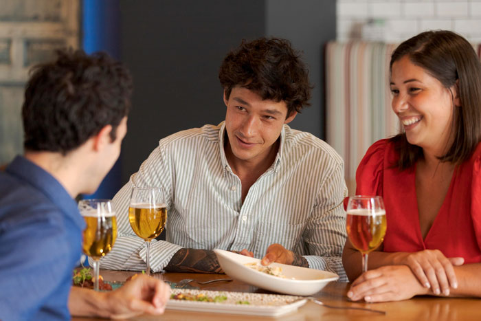 Three people sharing drinks and food at a table, highlighting a friend&rsquo;s compliment turning uncomfortable moment.