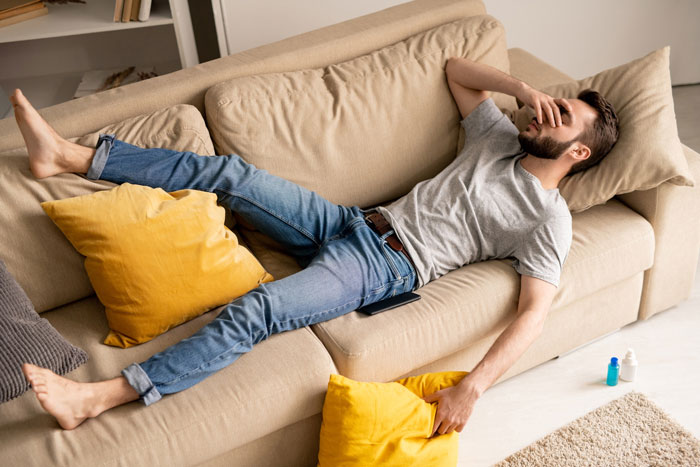 Man lying on sofa looking stressed, reflecting on friend&rsquo;s compliment turning uncomfortable and wife insisting on hotel stay.