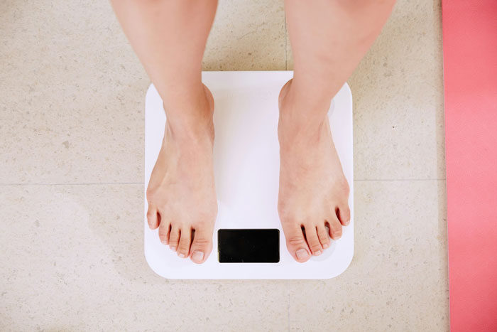 Person standing barefoot on a white digital weight scale, highlighting themes of weight loss and measurement.