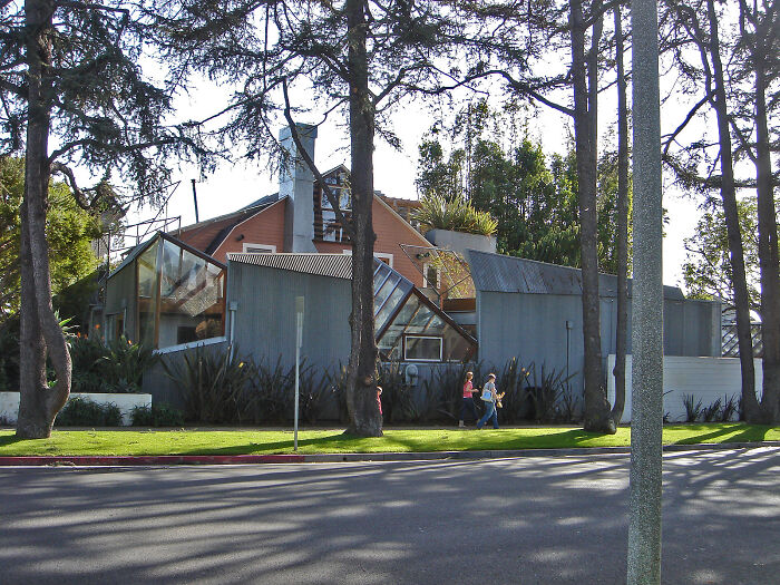 Modern iconic architectural homes with unique angular design surrounded by trees and people walking on sidewalk nearby
