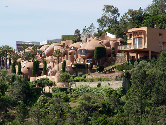 Iconic architectural homes with unique rounded shapes and numerous windows surrounded by lush greenery on a hillside.