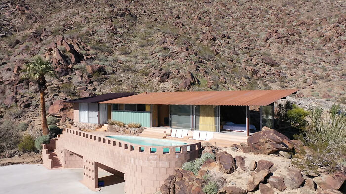 Modern desert iconic architectural home with flat roof and large windows built into rocky hillside with a pool on the terrace.