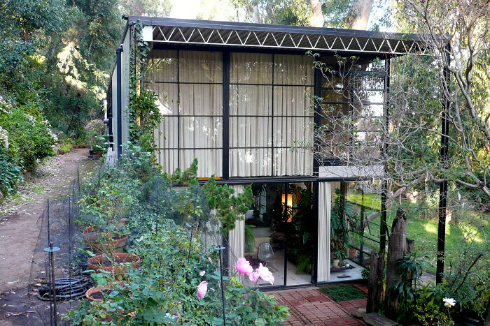 Modern iconic architectural homes with large glass windows surrounded by lush greenery and garden pathways.