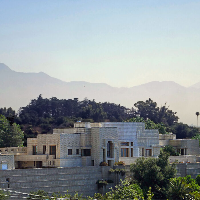 Modern iconic architectural homes surrounded by greenery and distant mountains under a clear sky.