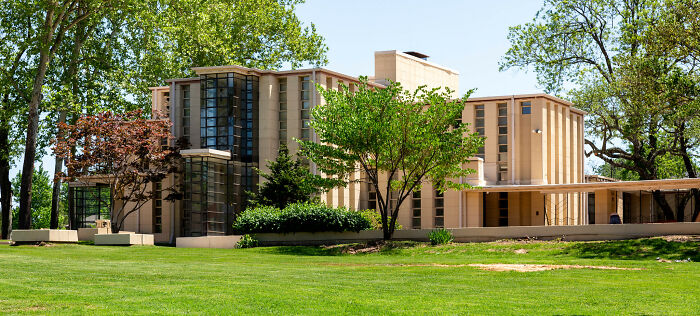 Modern iconic architectural home with large windows, surrounded by green trees and a manicured lawn.