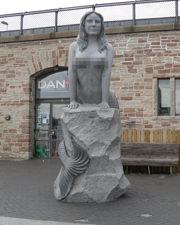 Mermaid statue made of stone depicting a female figure with a fish tail, located outdoors near a brick building. - 6