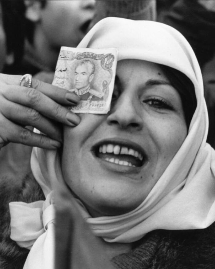 Black and white photo of a woman holding a vintage currency note over her eye, a weird history pic from the past.