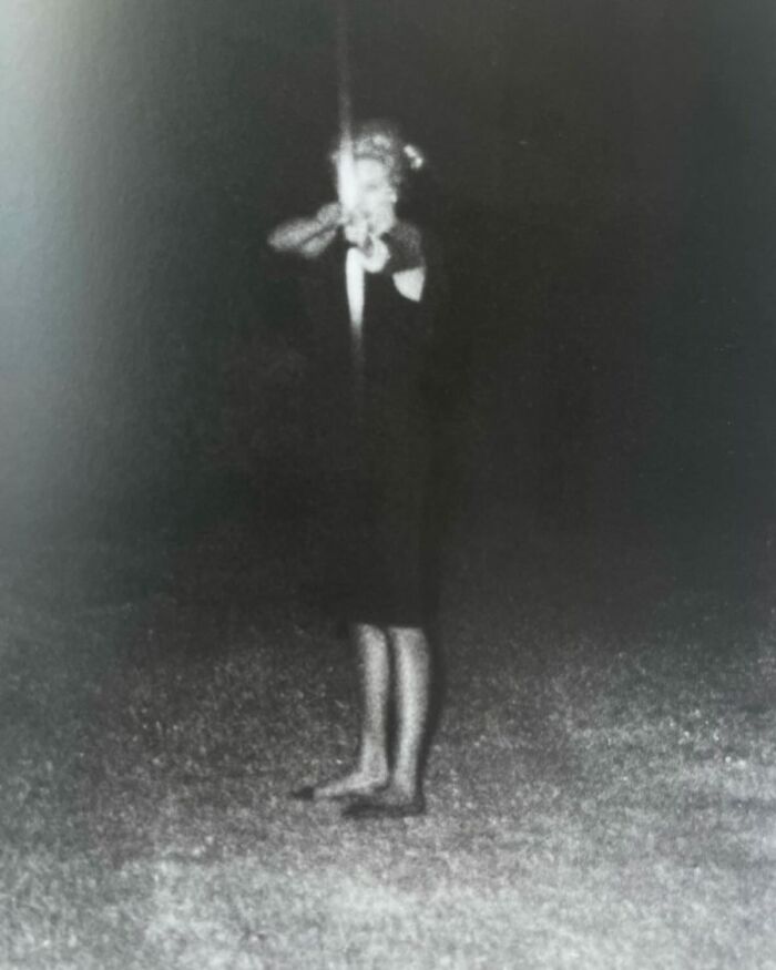 Black and white weird history pic of a barefoot woman aiming a gun at night in an outdoor setting.