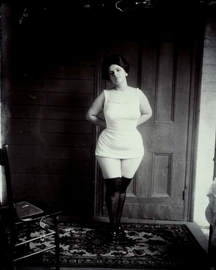 Vintage black and white photo of a woman in early 20th-century clothing standing indoors, a weird history pic revealing past fashion.