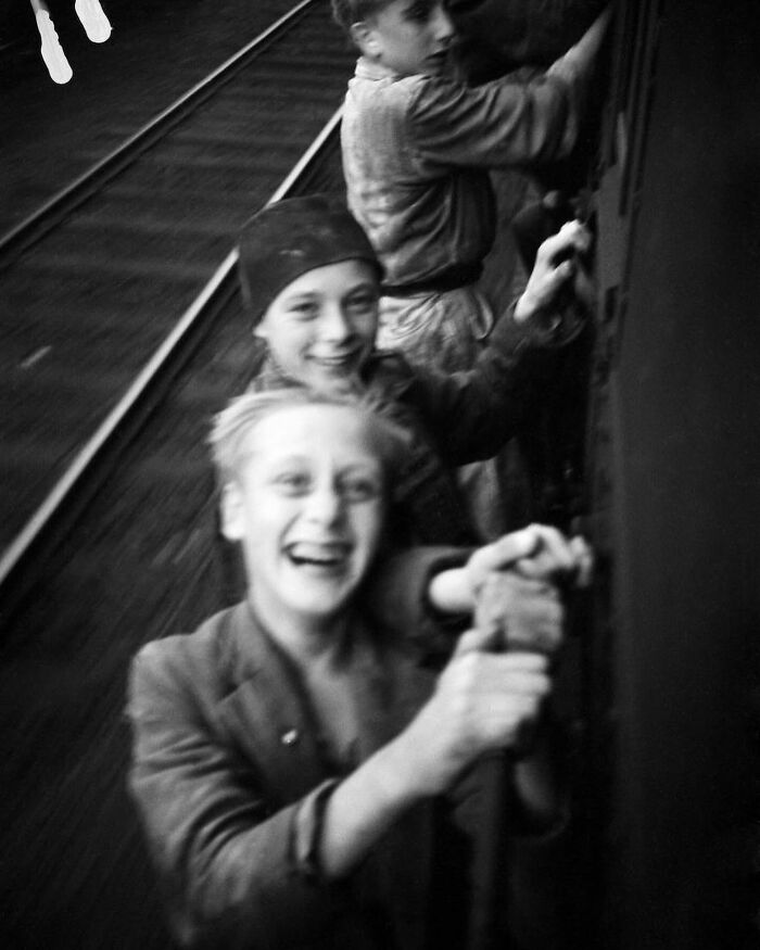 Three boys smiling and hanging onto a moving train, a rare weird history photo showing childhood adventures of the past.