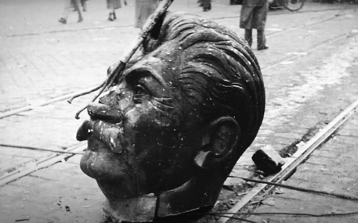 Large broken statue head of a man with a mustache lying on a street, a weird history picture showing the past uniquely.