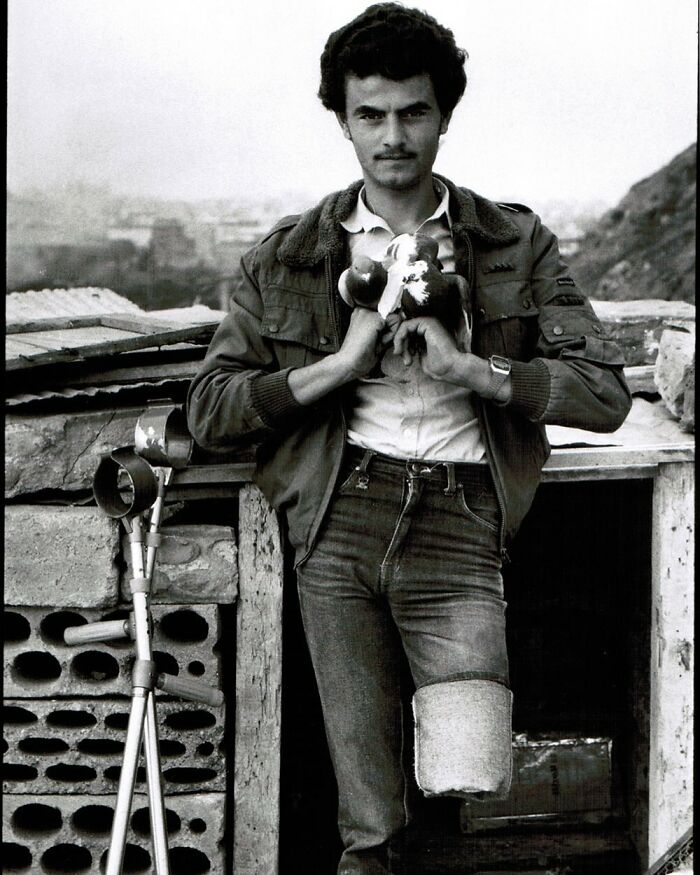 Young man with a leg prosthesis and crutches holding pigeons in a black and white weird history picture.
